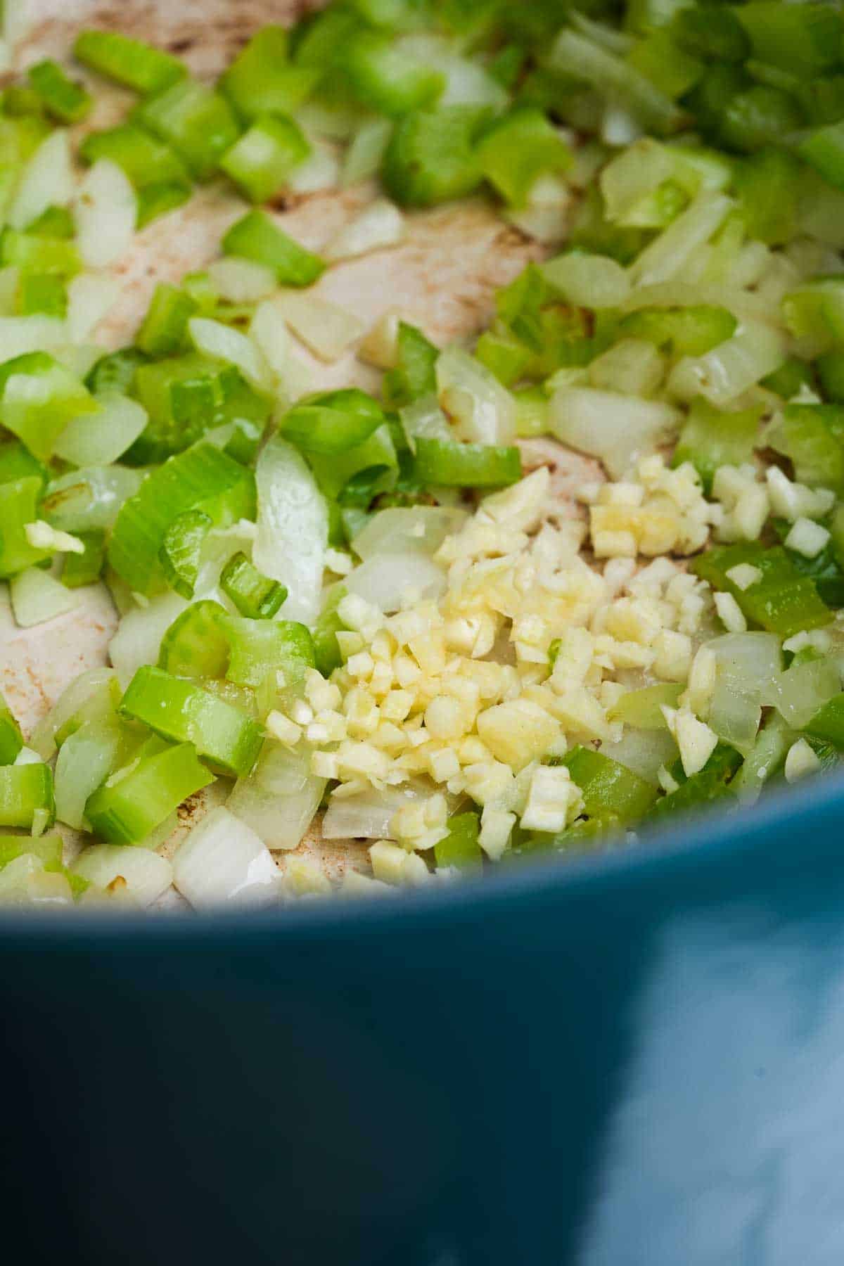 A pot of sauteing onions and celery gets garlic added to it.