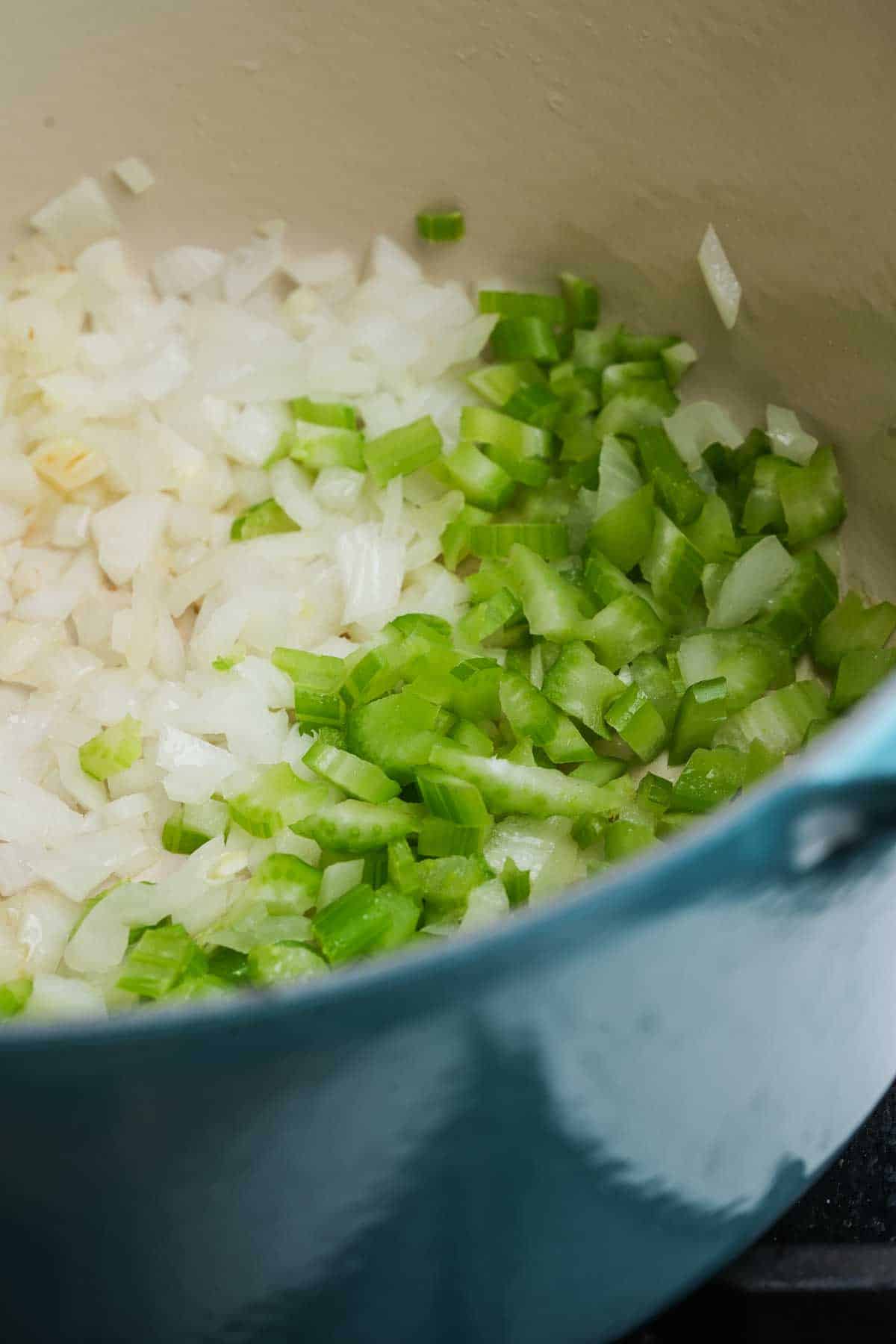 Onions and celery cooking in a pot on a stove.