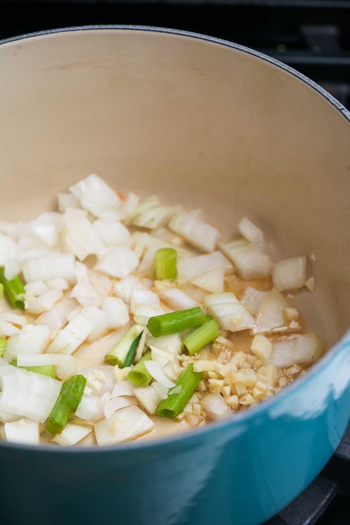 A pot filled with onions, scallions and garlic on the stove.