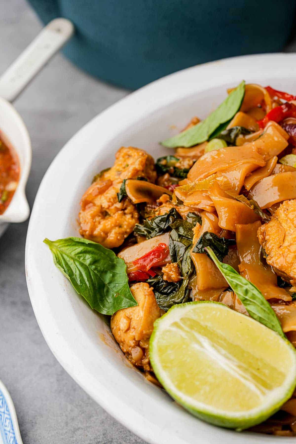 Pad Kee Mao in a white bowl with a lime wedge and Thai basil leaves.