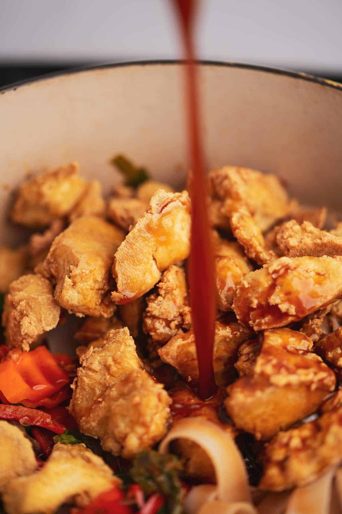 Stir fry sauce being poured over fried tofu in a pan.