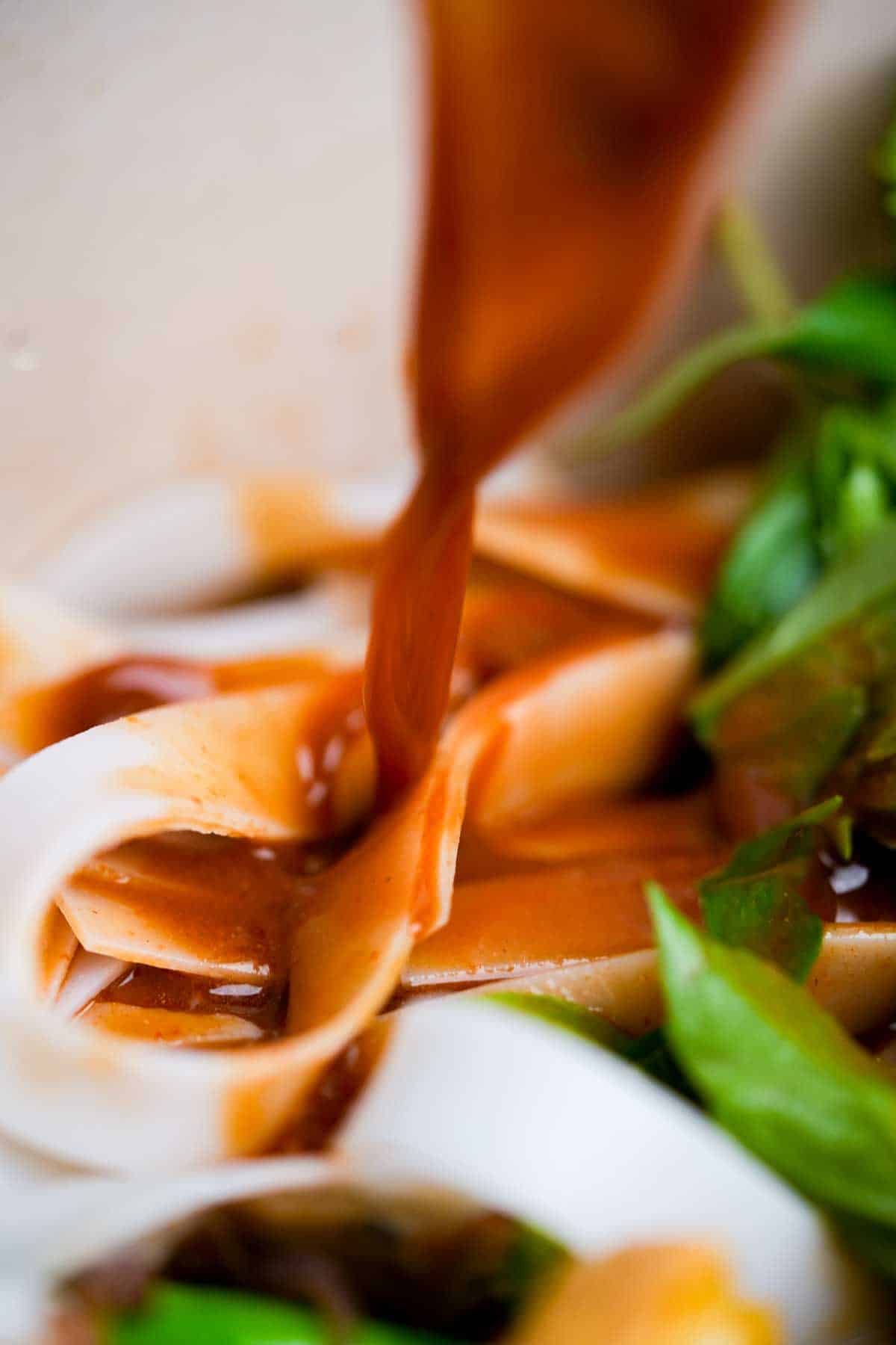 A sauce being poured over noodles and greens.