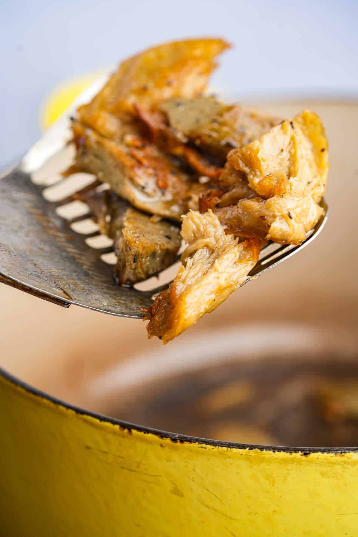 A slotted spoon is being used to flip seitan pieces in a yellow pot.