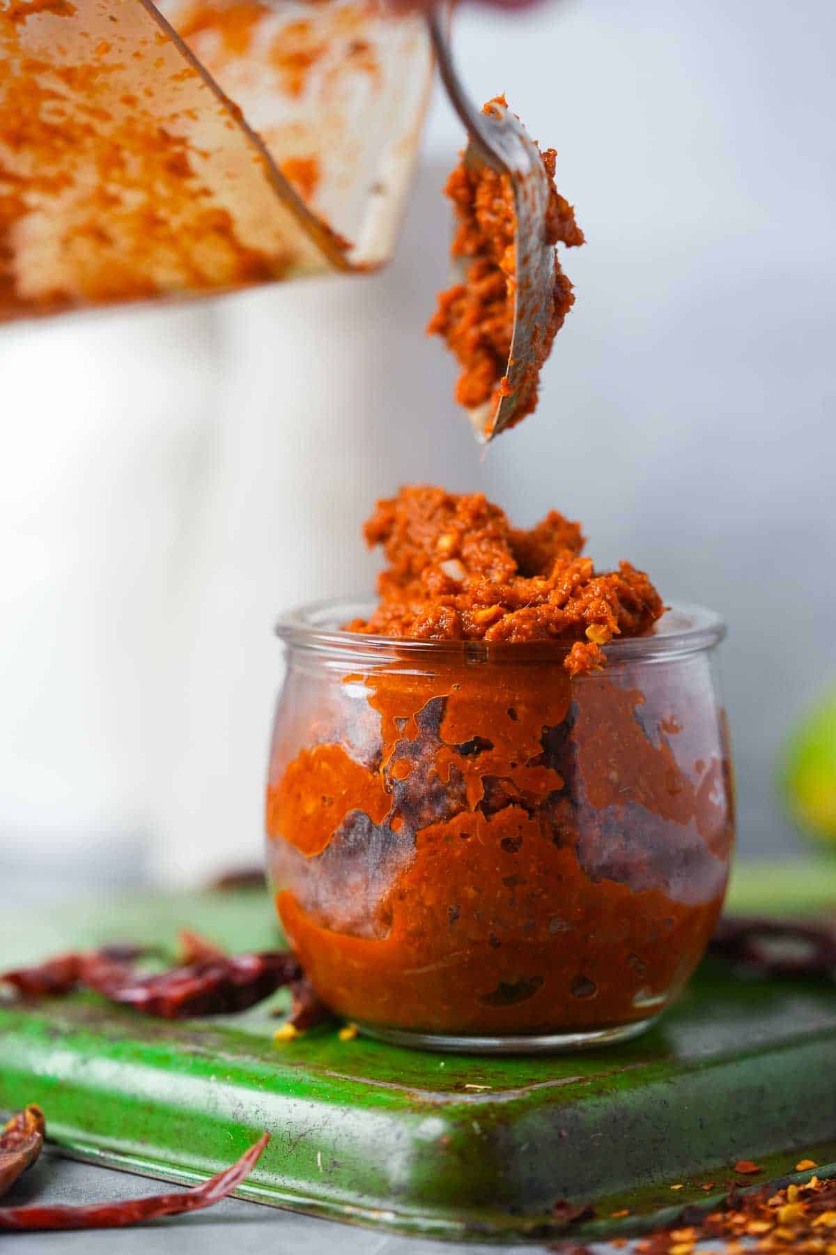 A spoon is being used to put red curry paste into a jar.