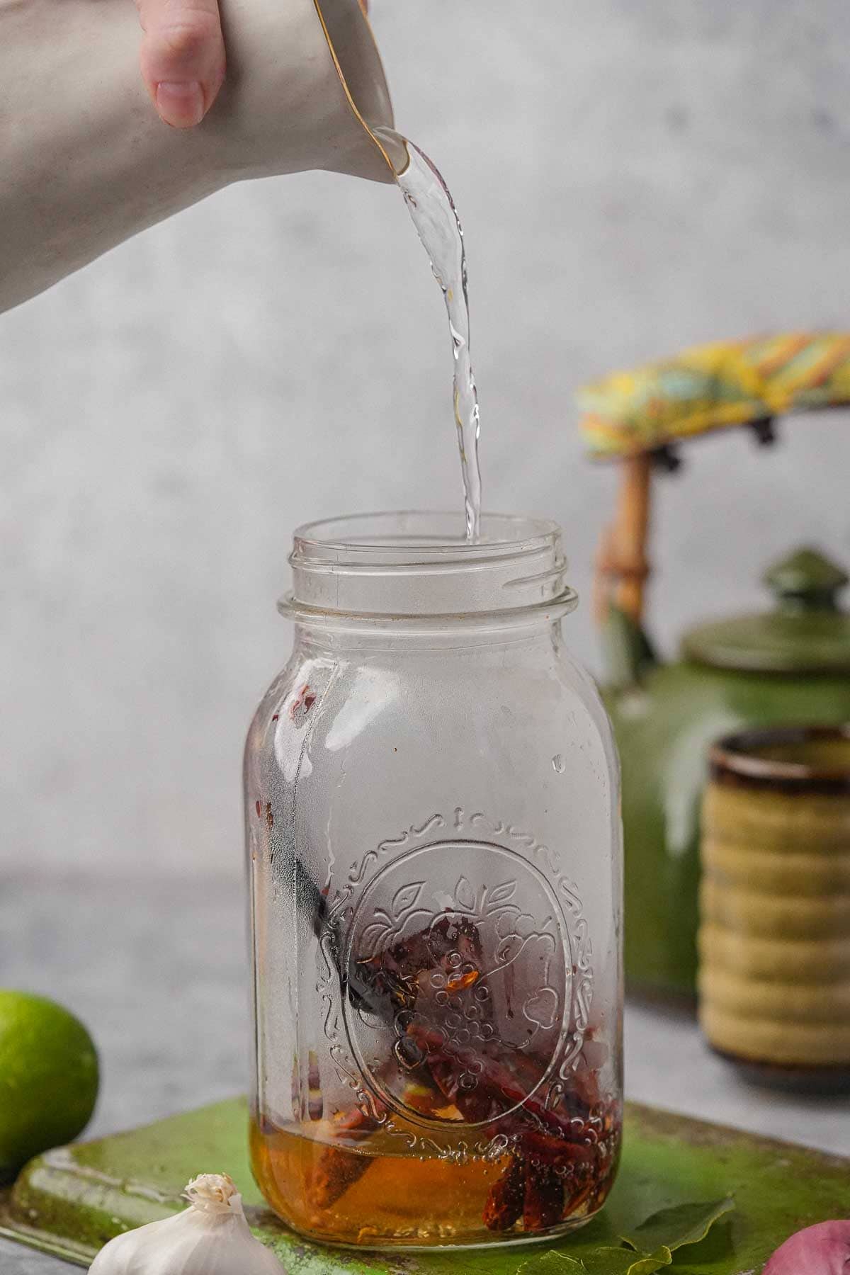 A person pouring a liquid into a mason jar filled with dried chilies.