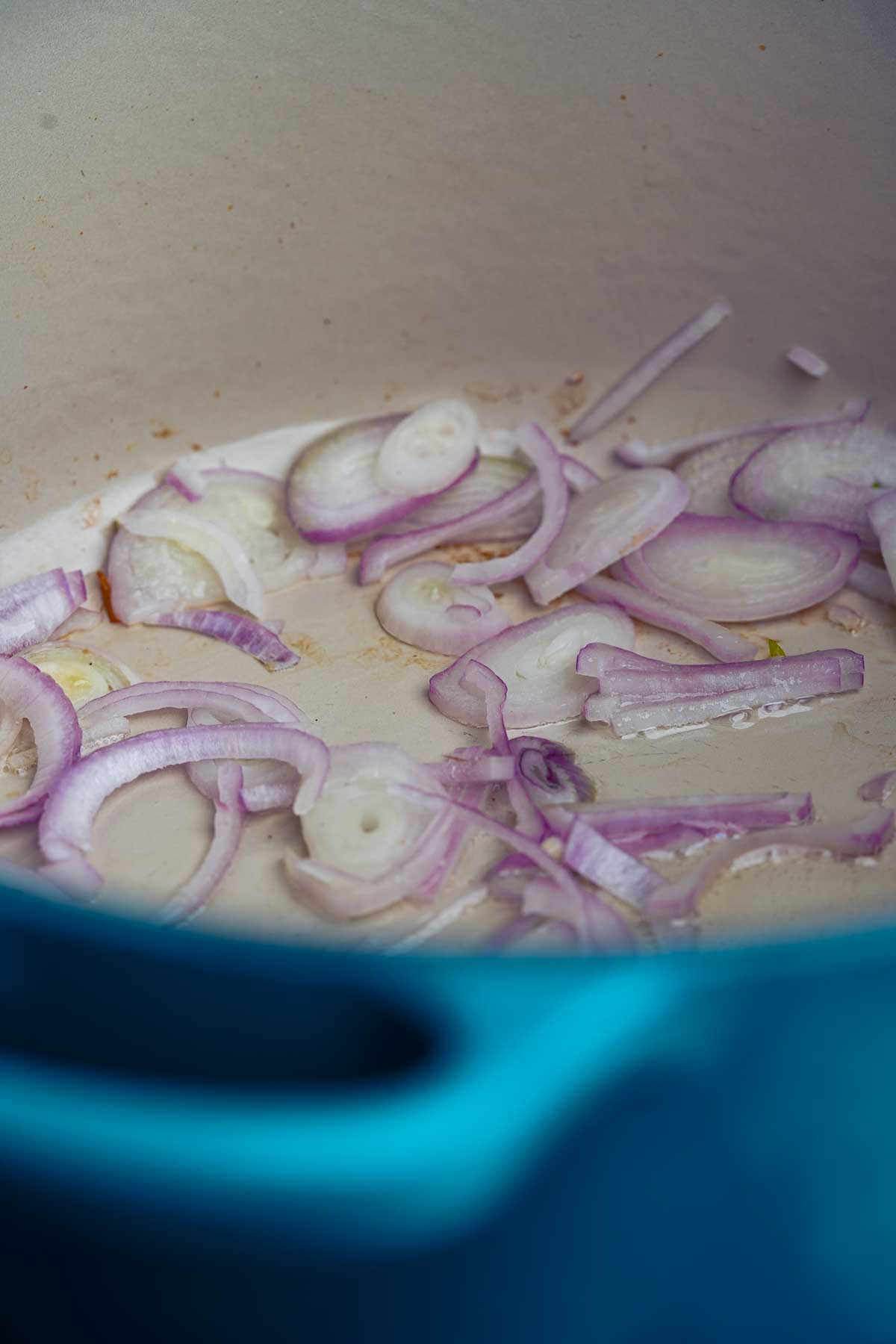 A pot of shallots being cooked in a blue pot.