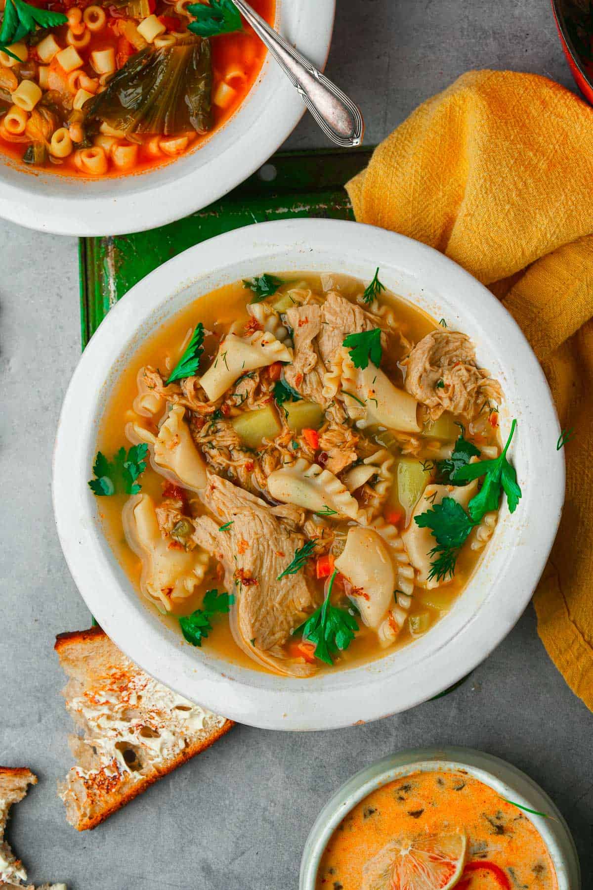 A bowl of vegan chicken noodle soup, a bowl of tom kha and a bowl of escarole and bean soup with bread.