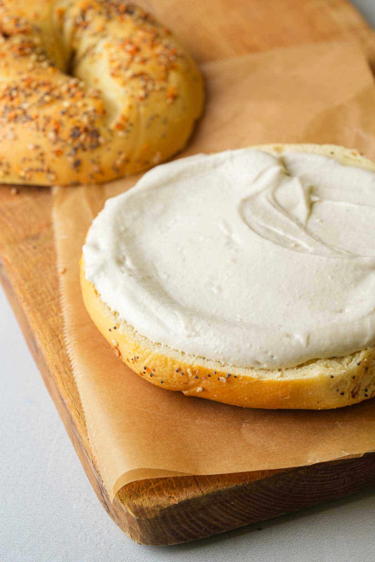 A bagel with cream cheese on a cutting board.