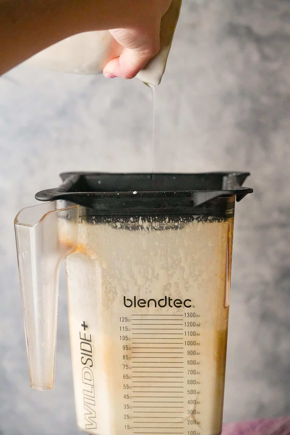 A person drizzling oil into a blender which is running.