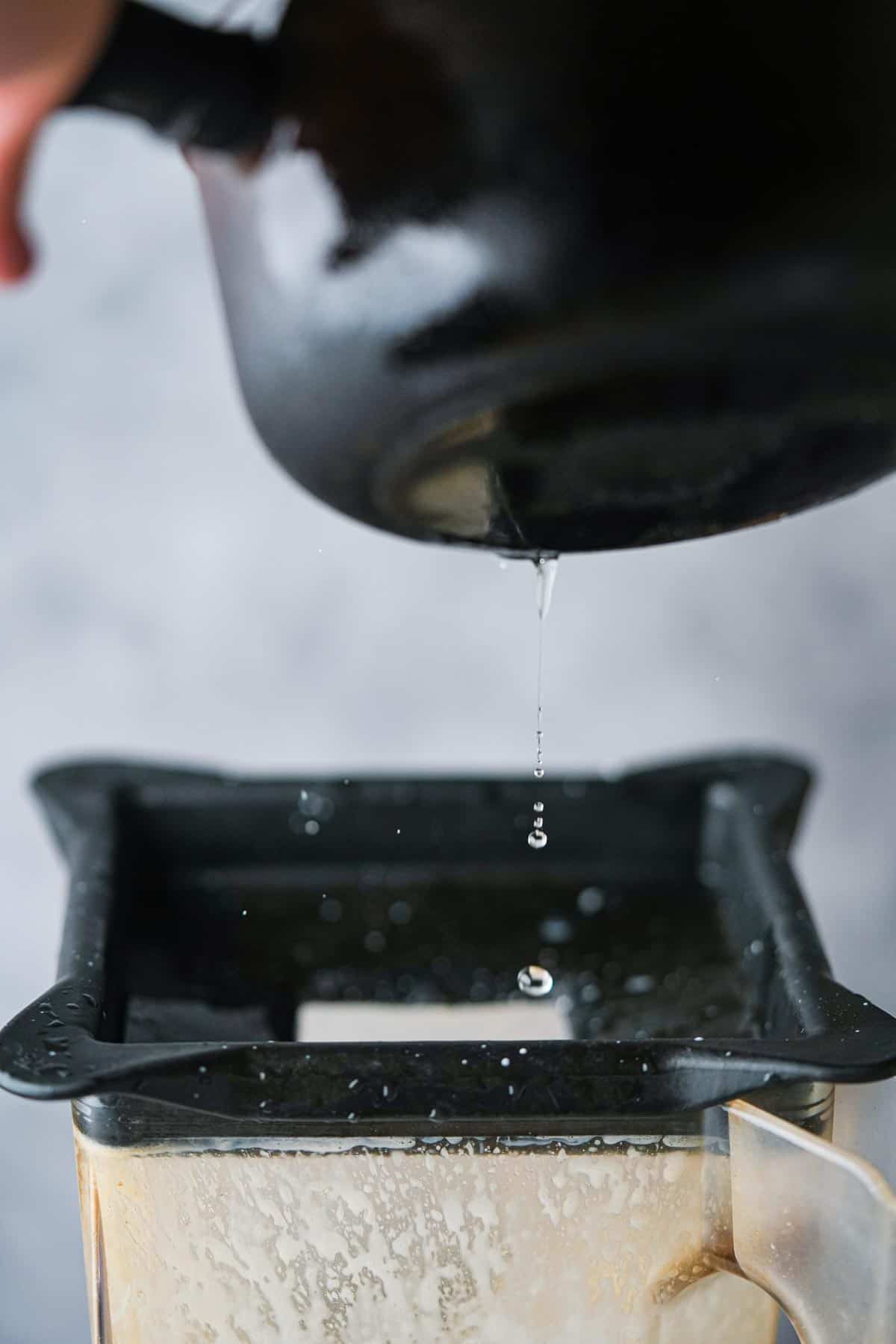 A person drizzling oil into a blender as it runs.