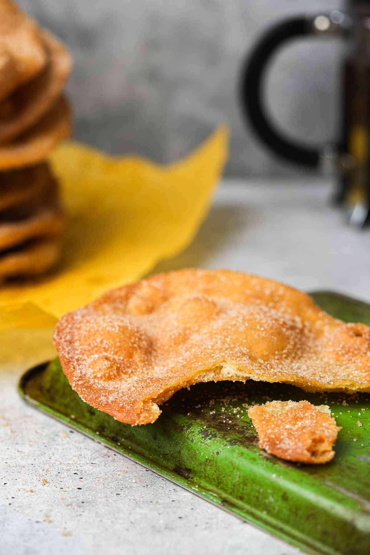 A stack of fried bunuelos on a tray with a cup of coffee.