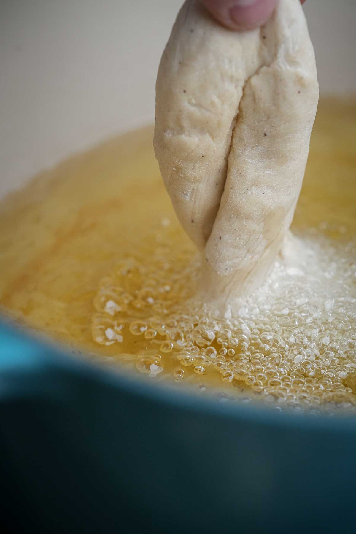 A person adding a twisted donut to a boiling pot of oil.