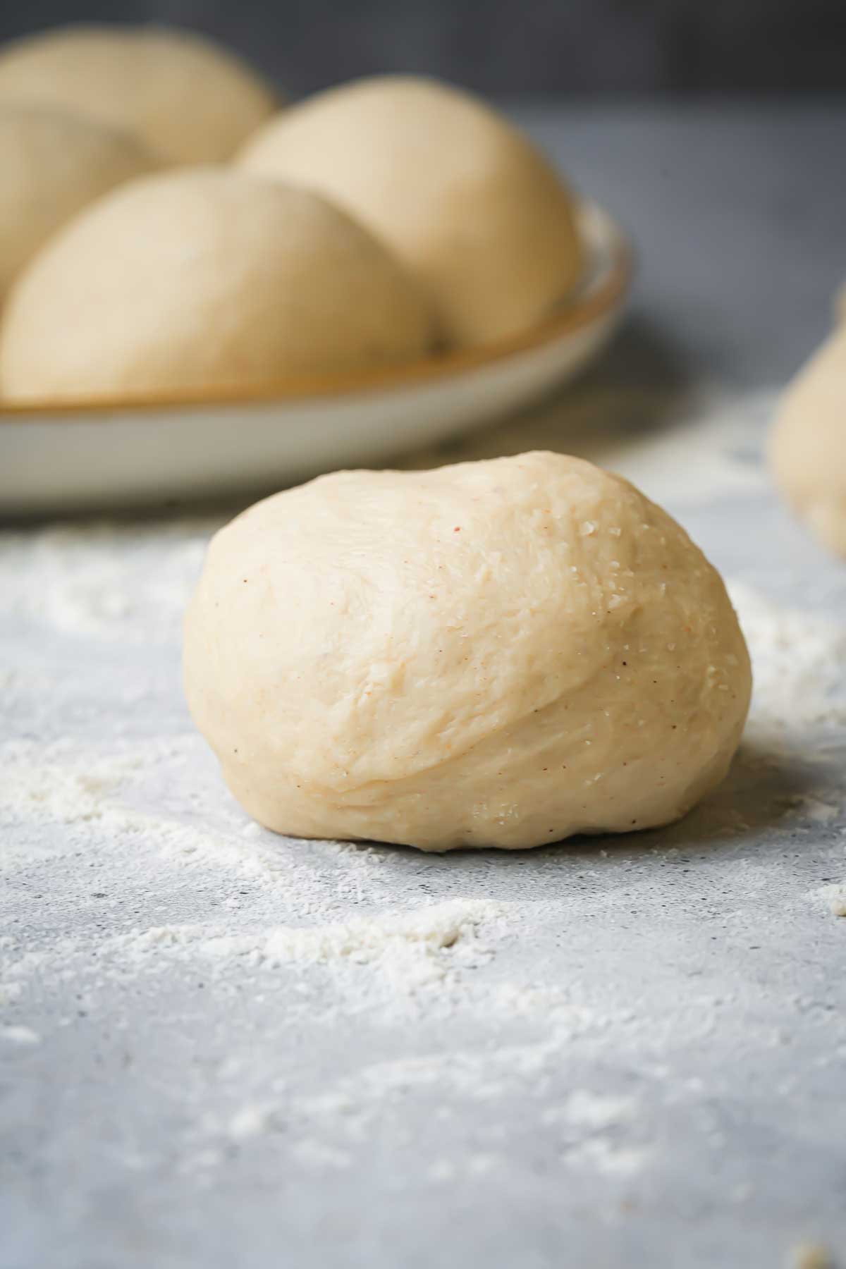 A plate of small dough balls and a few dough balls on a work surface.