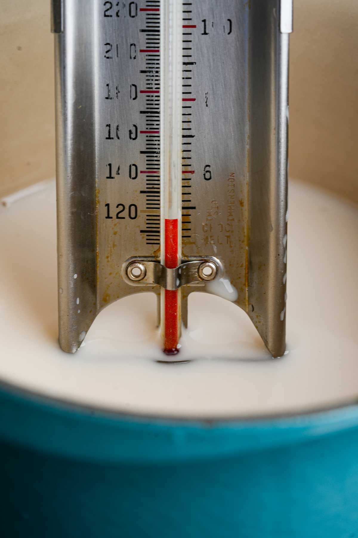 A close up of a thermometer in warming plant-based milk in a blue pot.