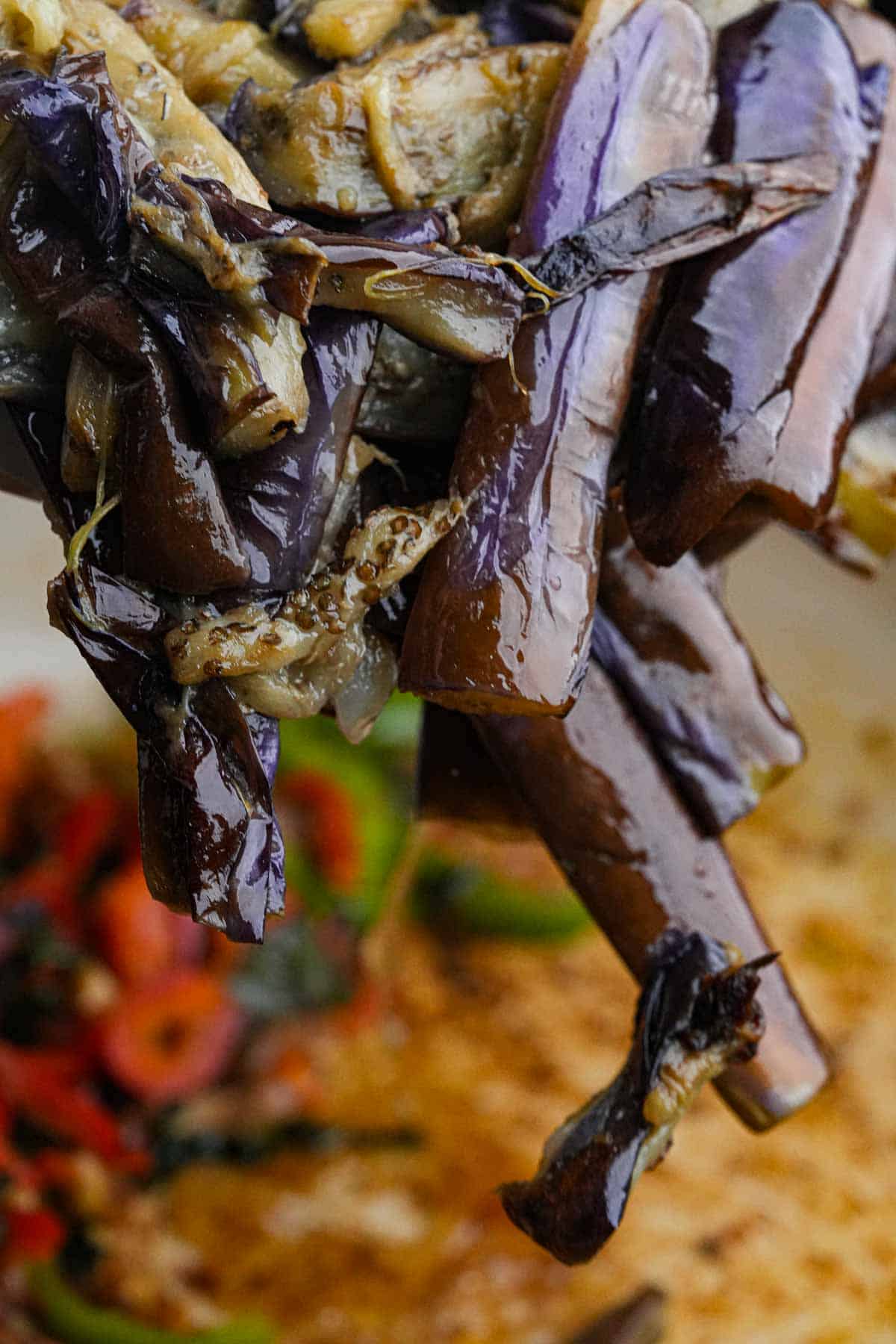 Freid eggplant being added to the stir frying vegetables in a pan.