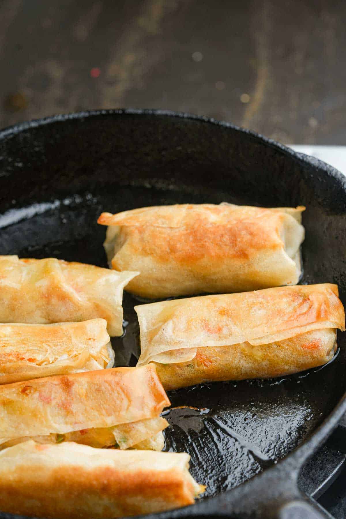 Fried spring rolls cooking in a cast iron skillet.