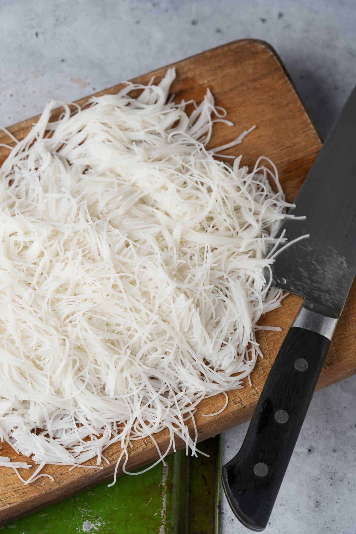 Chopped noodles on a cutting board with a knife.