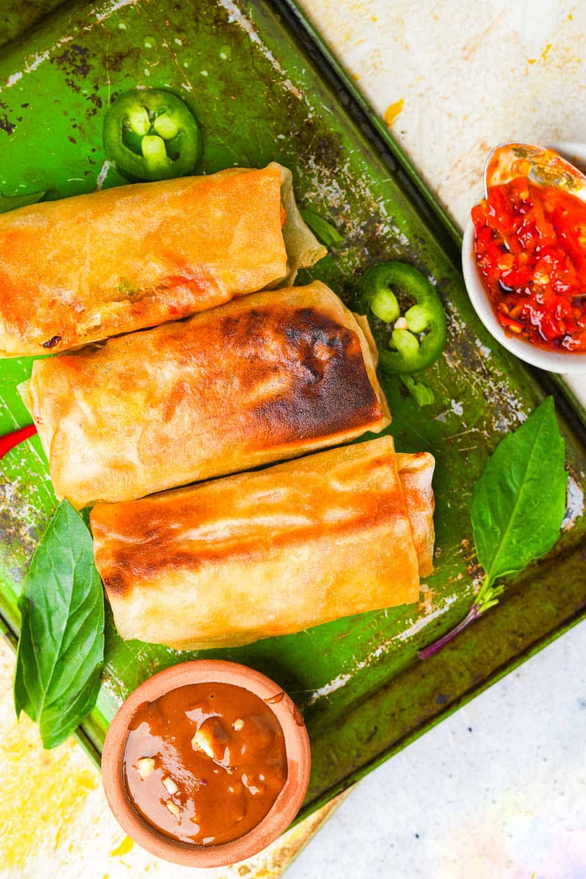 Thai spring rolls on a green tray with dipping sauce.