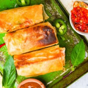 Thai spring rolls on a green tray with sauce.