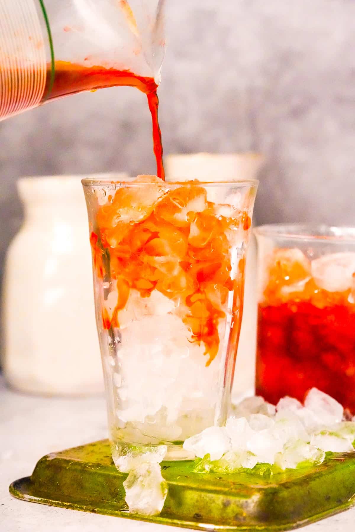 A glass pitcher of Thai iced tea being poured into a glass.
