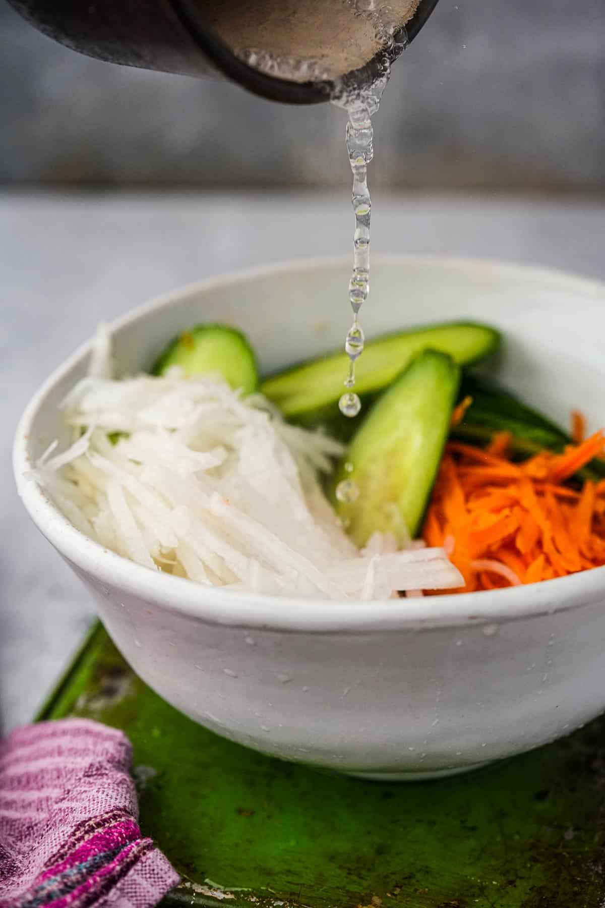 Hot brine is poured into a bowl of vegetables.