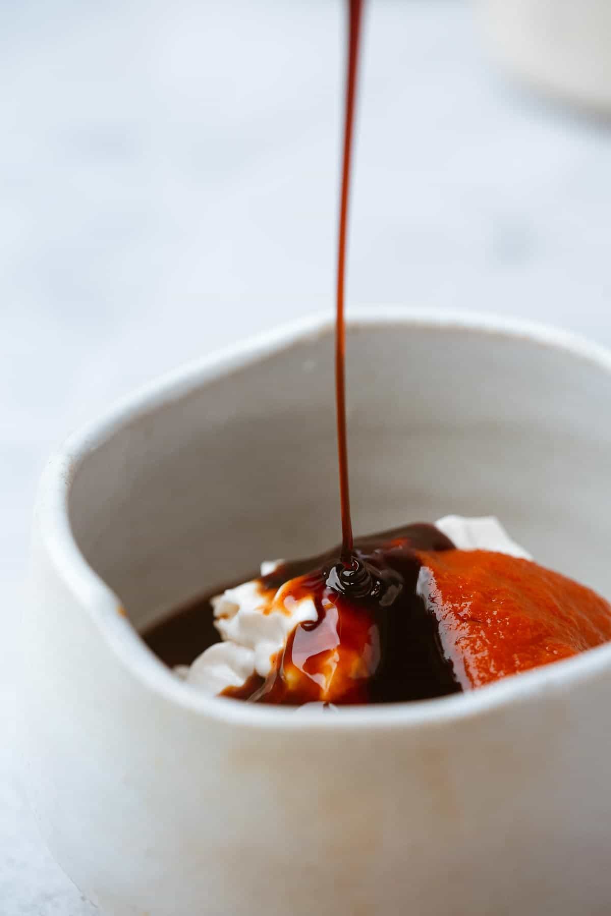 Hoisin sauce is being poured into a white bowl with sriracha and vegan mayo.