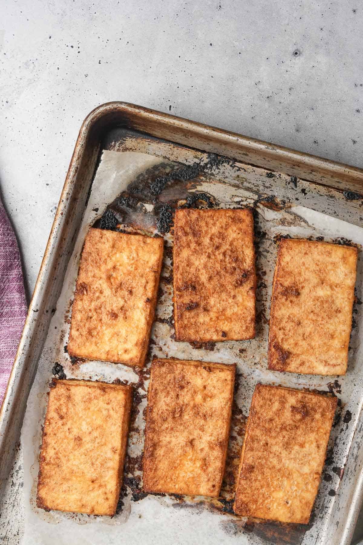 Six slices of of roasted tofu on a baking sheet.