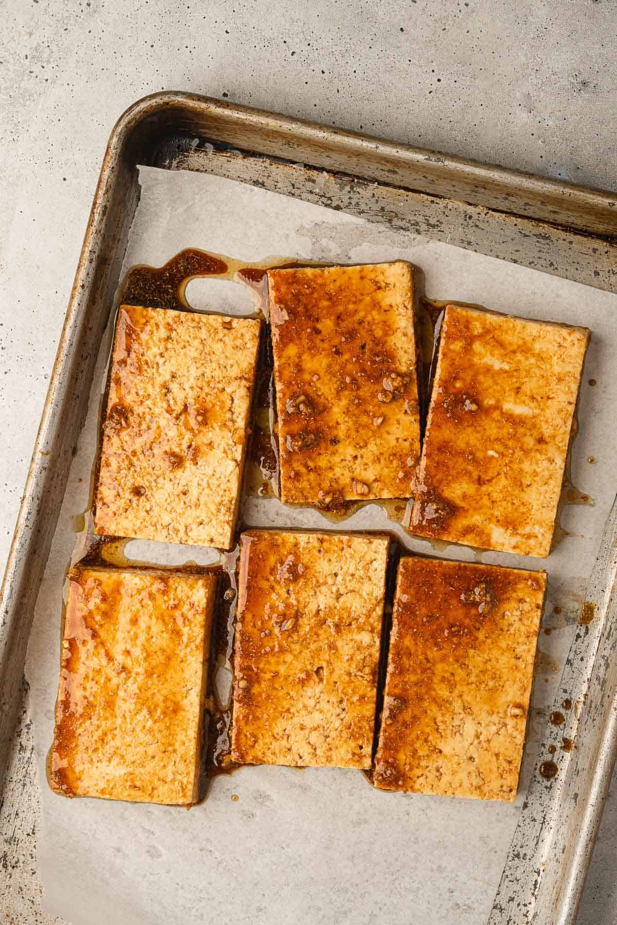 Six pieces of tofu on a baking sheet.