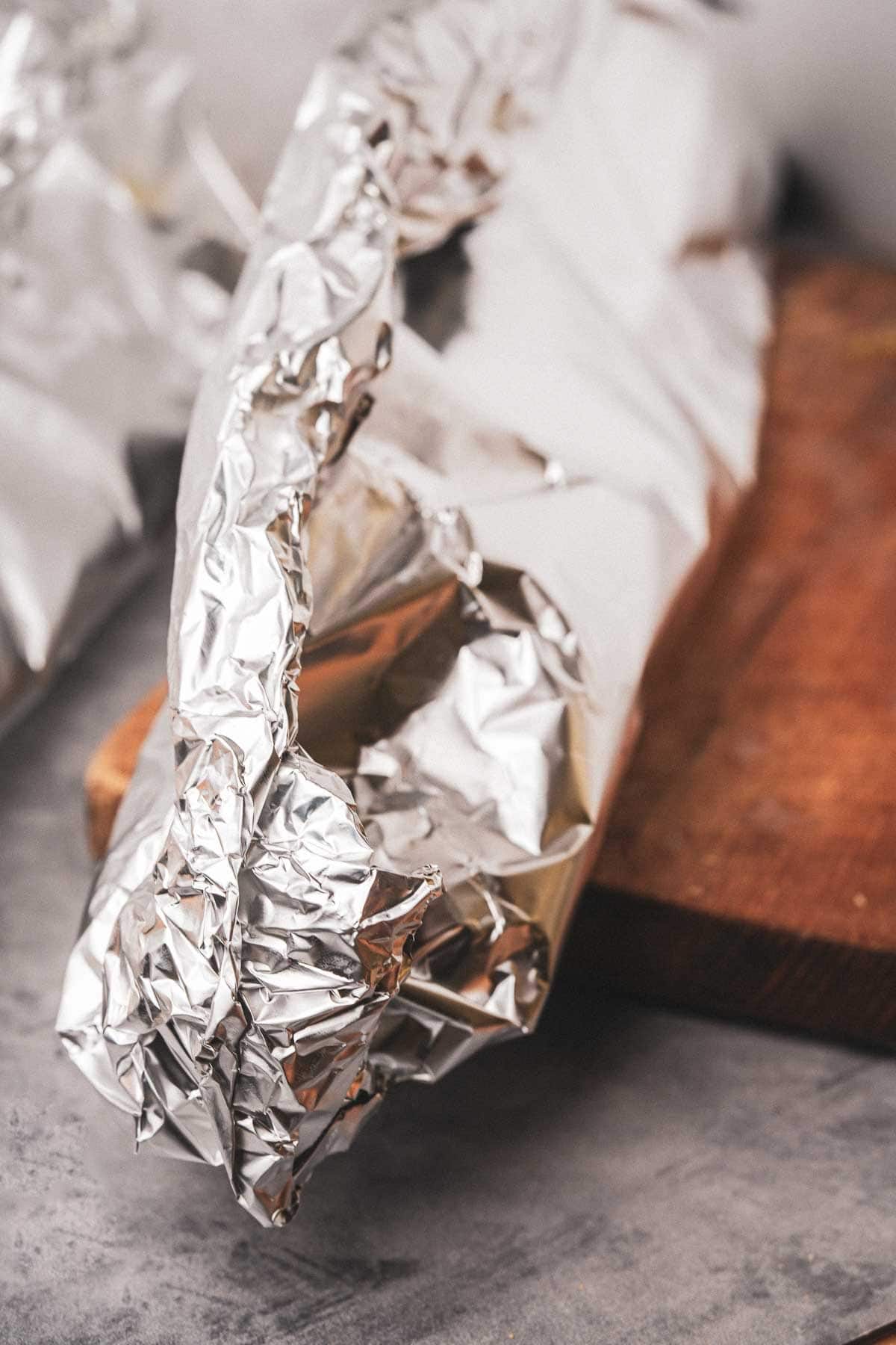A piece of aluminum foil wrapped vegan garlic bread sitting on a cutting board.