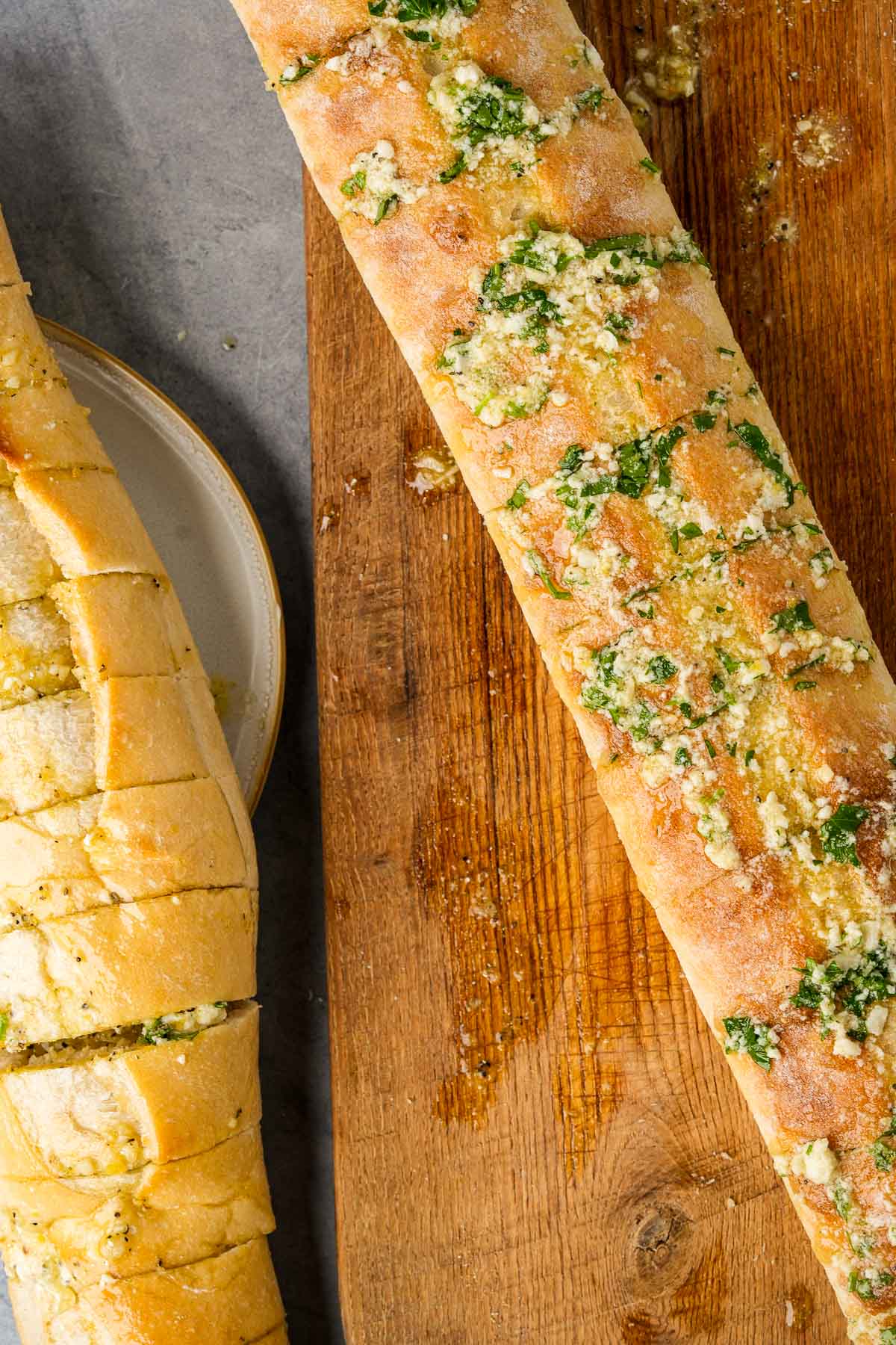 Two loaves of unbaked vegan garlic bread on a cutting board.