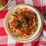 Spaghetti and vegan meatballs on a red and white checkered tablecloth.
