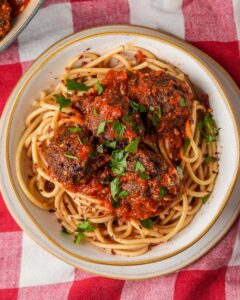 Spaghetti and vegan meatballs on a red and white checkered tablecloth.