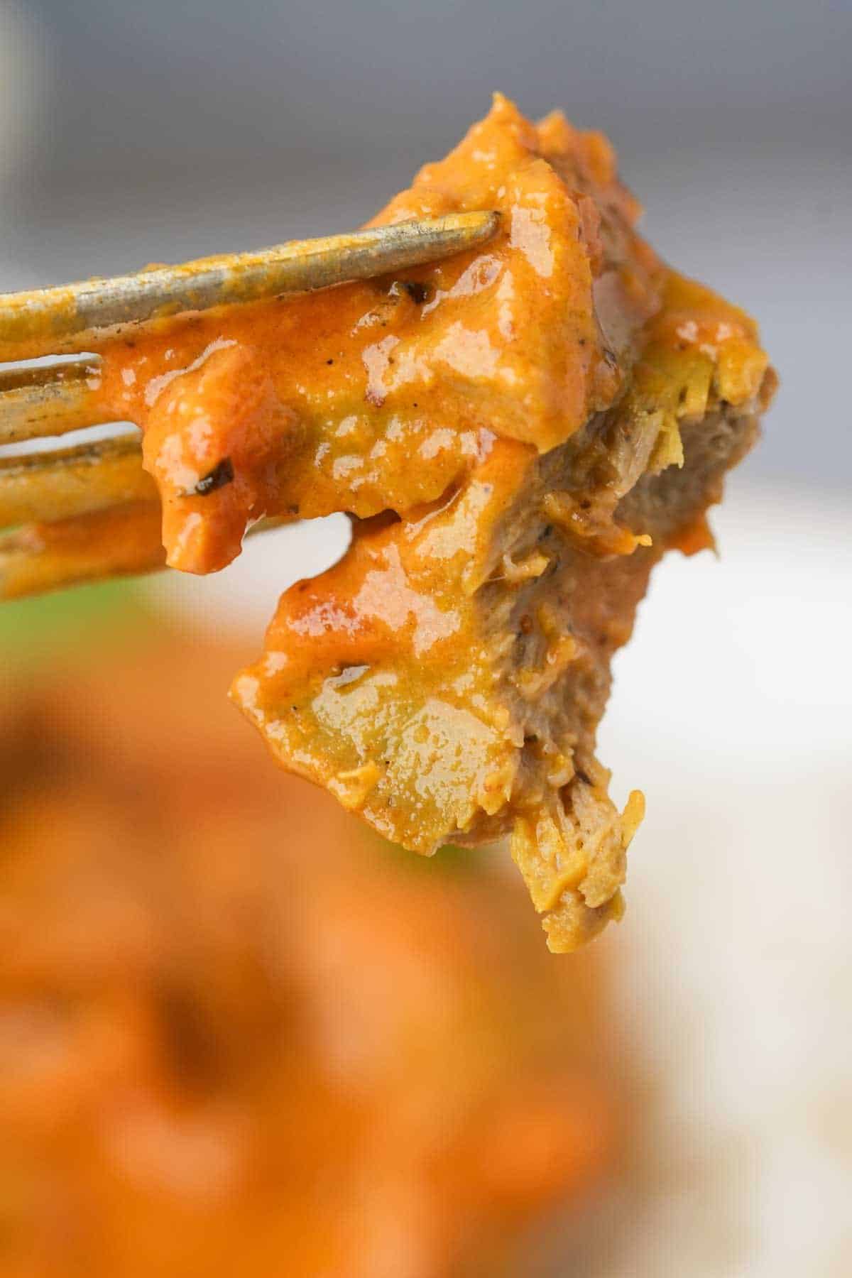 A fork is holding a piece of seitan tika masala over a plate.