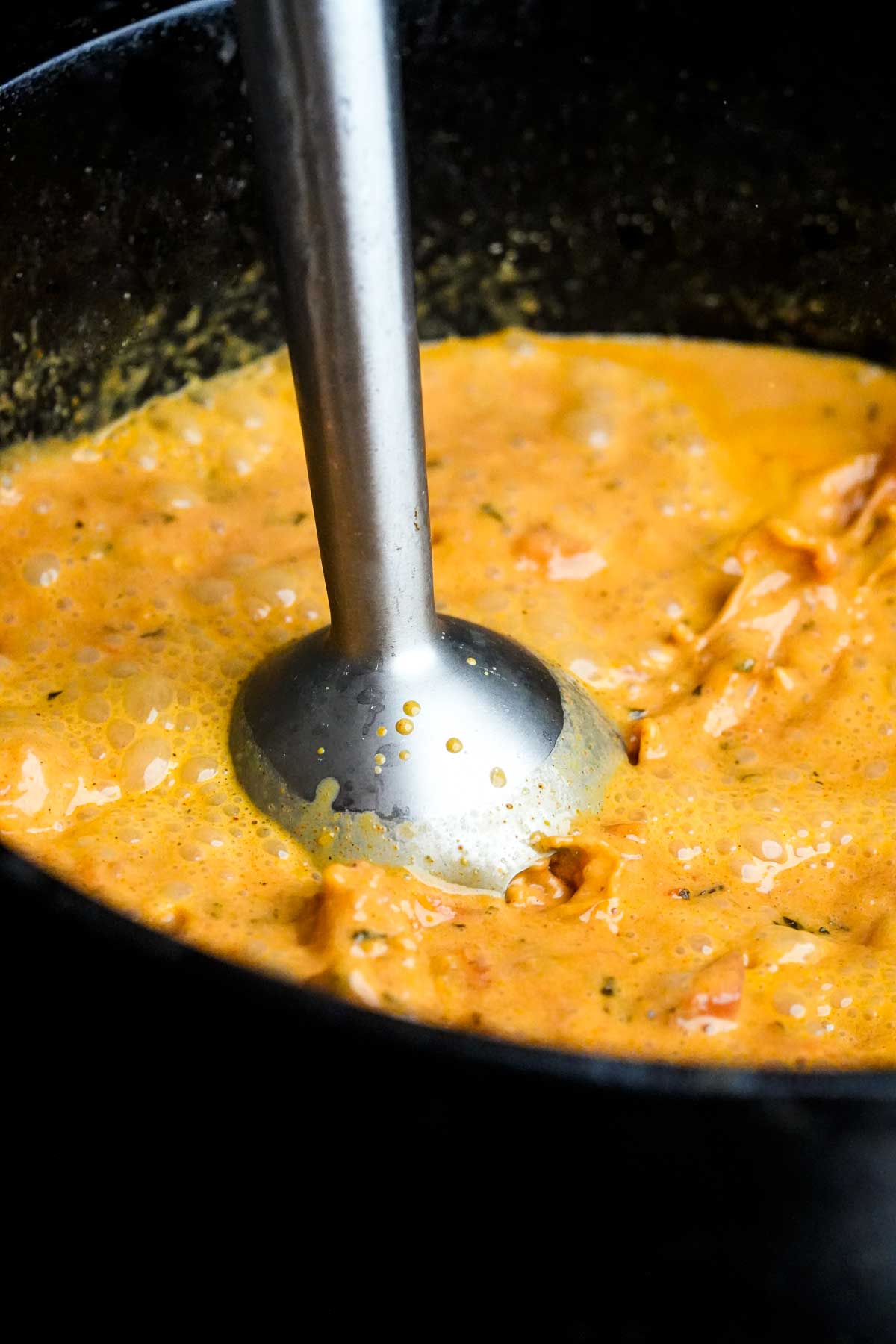 An immersion blender is being used to puree a sauce in a pan.