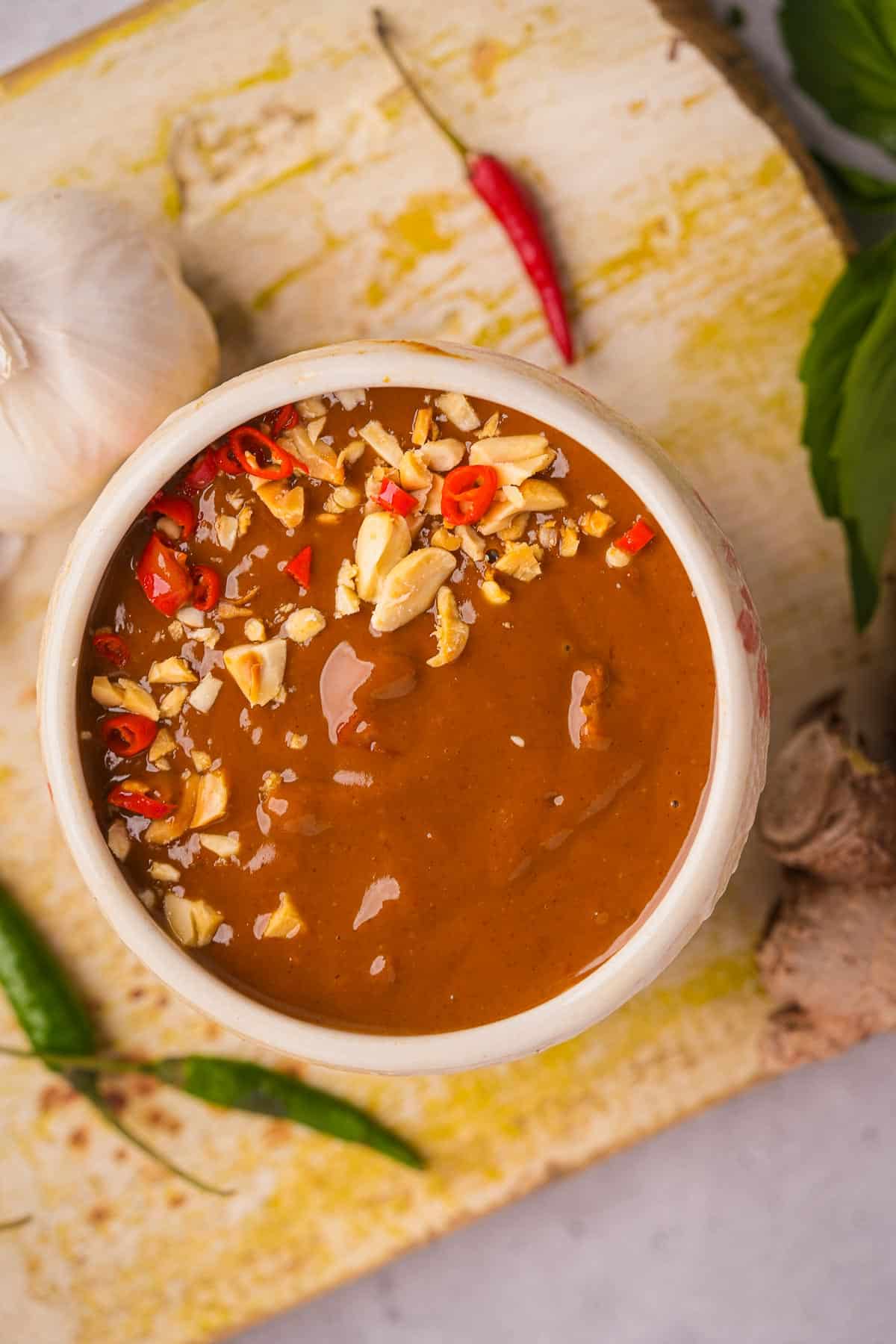 Vietnamese peanut sauce in a bowl on a wooden board with garlic and chilies on it.