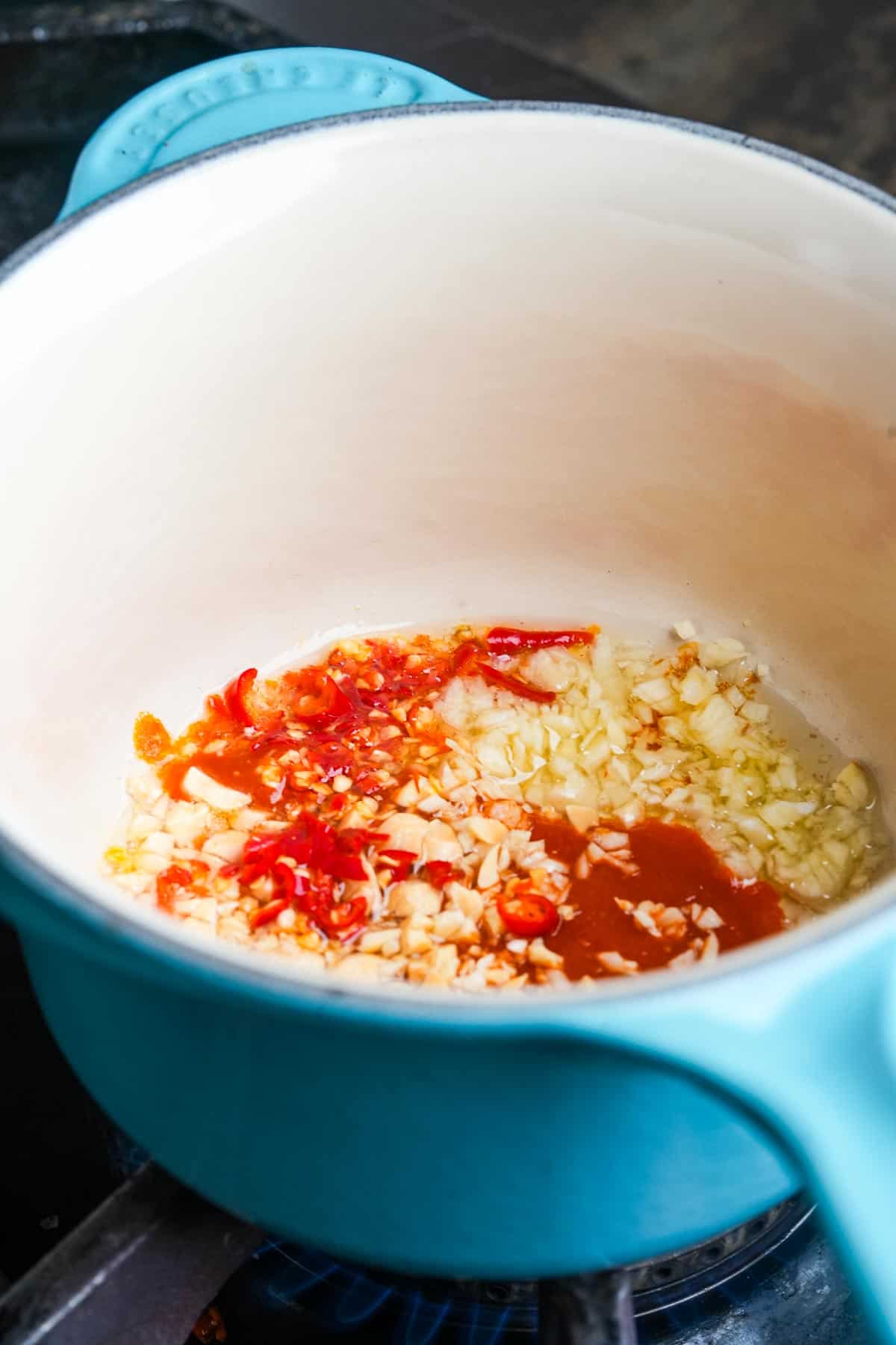 A blue pot with garlic, chilies, and hot sauce on top of a stove.