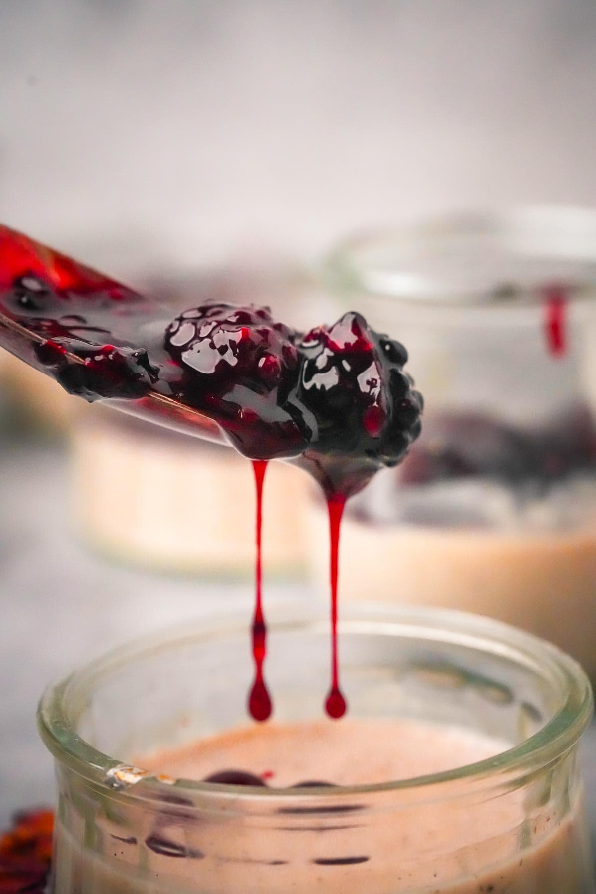 A spoon is dripping blackberry sauce into a jar of Coconut Panna Cotta.