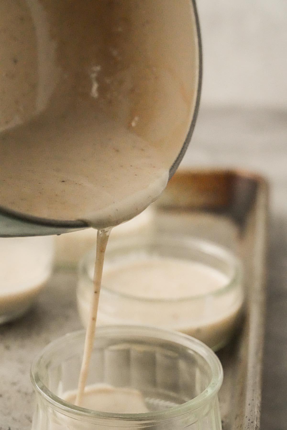 A cup of liquid Coconut Panna Cotta being poured into a set of glasses.