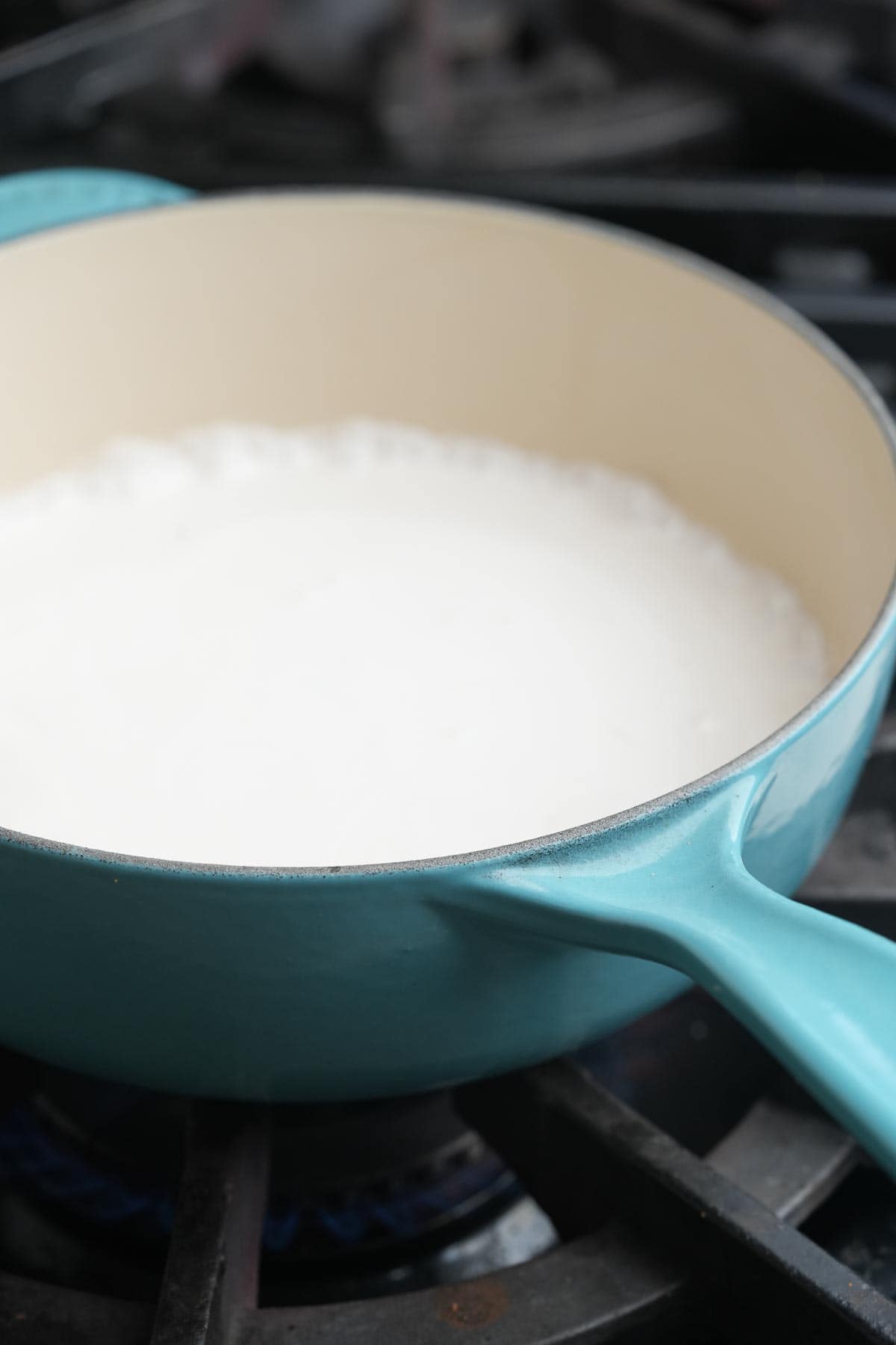 A blue pan warming coconut milk on a stove top.