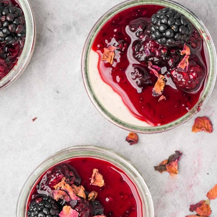 Three jars of blackberry sauce topped vegan panna cotta with rose petals on top.