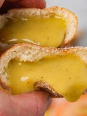 A person holding Vegan Bomboloni with a yellow pastry cream dripping out of it.