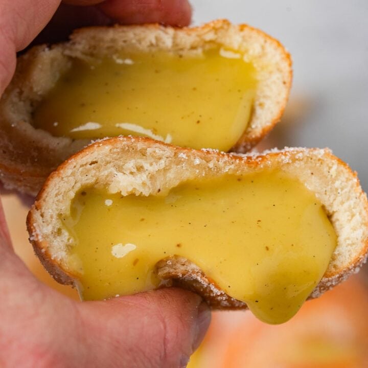A person holding Vegan Bomboloni with a yellow pastry cream dripping out of it.