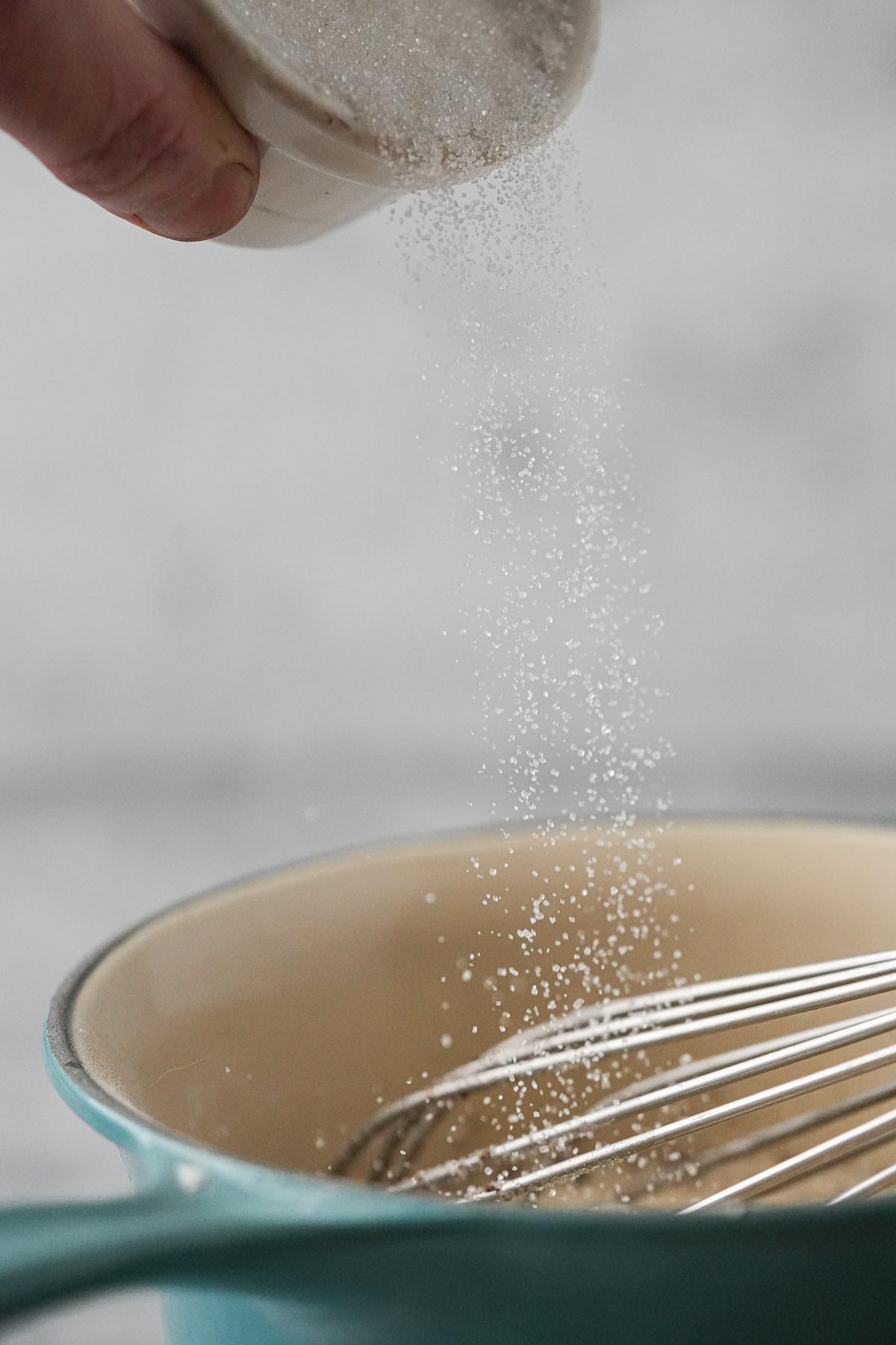 A person is pouring sugar into a bowl.