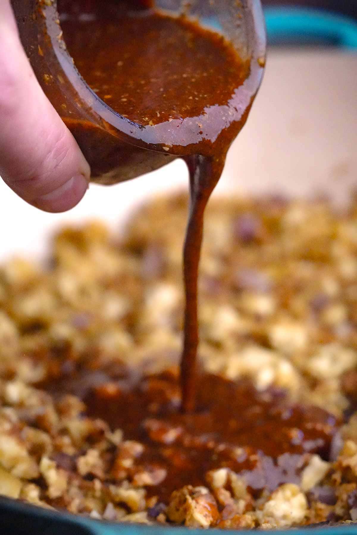 A person is pouring sauce on a skillet.