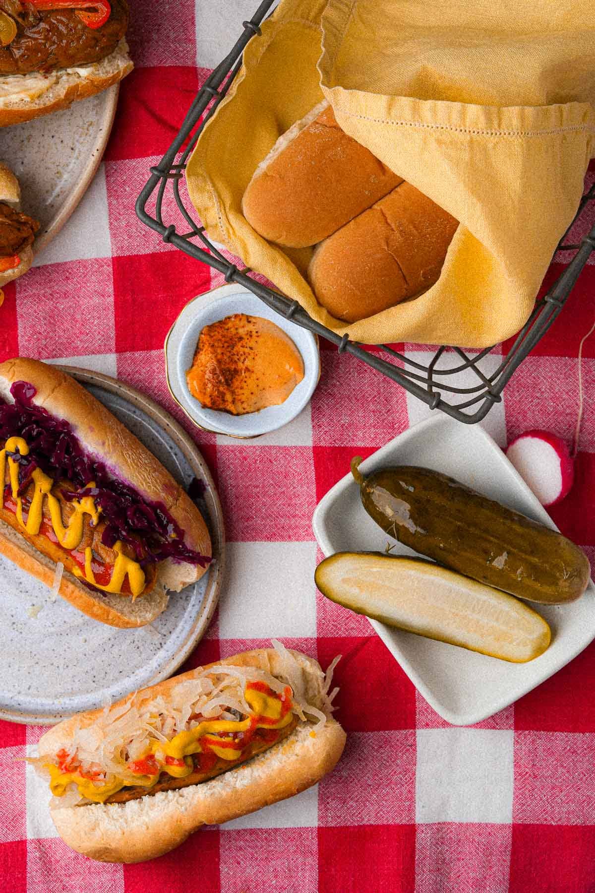 A red and white checkered tablecloth with vegan hot dogs and pickles on it.