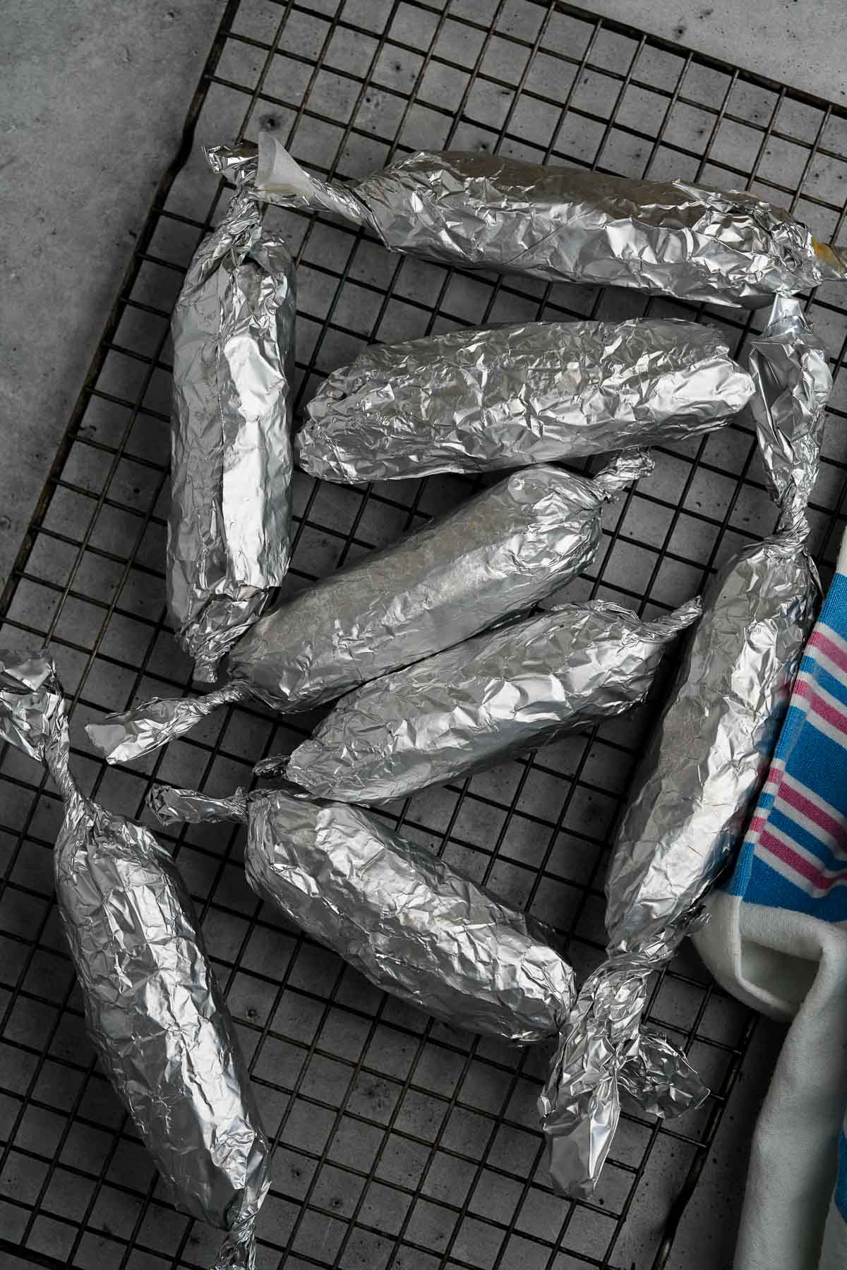 A group of wrapped hot dogs on a cooling rack.