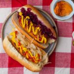 Two hot dogs on a red and white checkered tablecloth.
