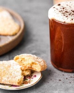 A cup of coffee and vegan ladyfinger cookies on a plate.