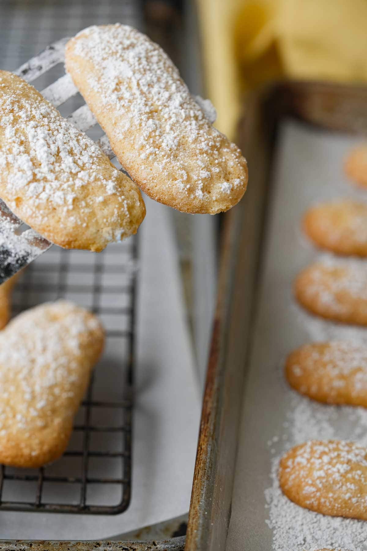 Powdered sugar coated vegan ladyfinger cookies being placed on a wire rack.
