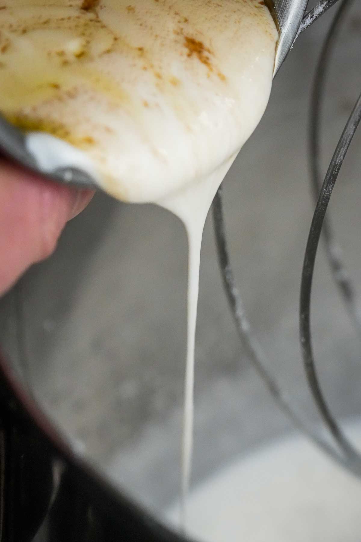 A person pouring vegan yogurt and vanilla into a mixing bowl.